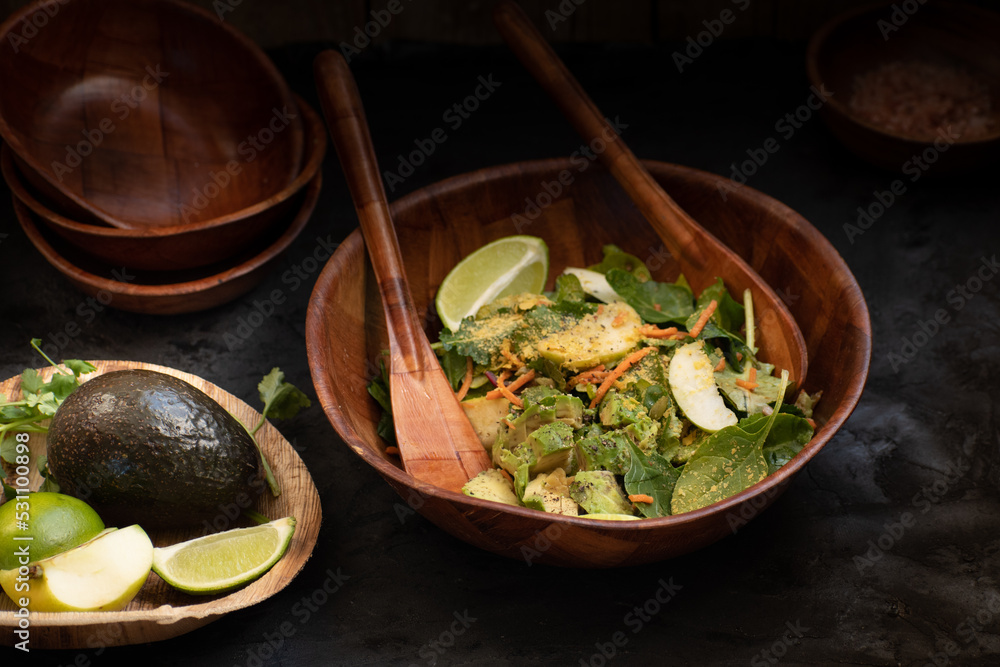 Avocado, apple slices and spinach salad in wooden bowl