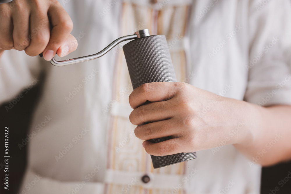 Barista is grinding coffee beans with manual stainless steel grinder to make black coffee machine, brewing equipment or coffee drip set Dripper on a wooden table In the kitchen at home in the morning Barista is grinding coffee beans with manual stainless steel grinder to make black coffee machine, brewing equipment or coffee drip set Dripper on a wooden table In the kitchen at home in the morning