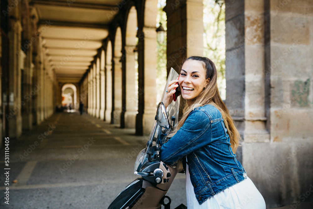 Fototapeta premium Young smiling woman on a motorbike talking on a red smartphone