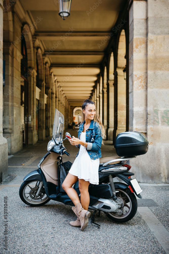 Young smiling woman on a motorbike using a red smartphone