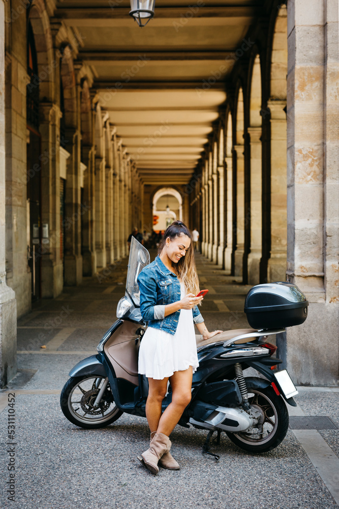 Young smiling woman on a motorbike using a red smartphone