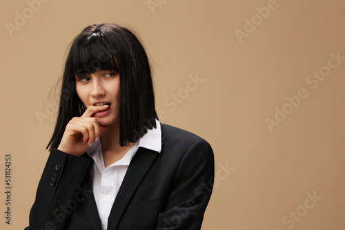 Pensive thoughtful pretty brunet lady in classic suit bites finger look aside posing isolated on pastel beige studio background. Copy space Banner Offer. Pulp Fiction concept. Fashion Cinema