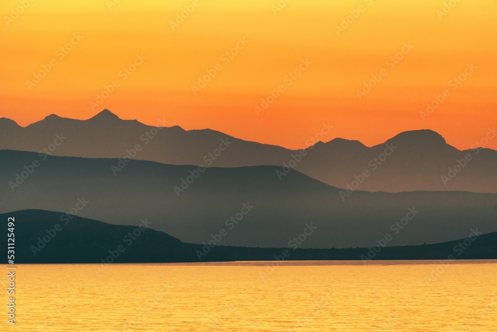 Illustration of a mountain range behind a seascape at sunset - obrazy, fototapety, plakaty 