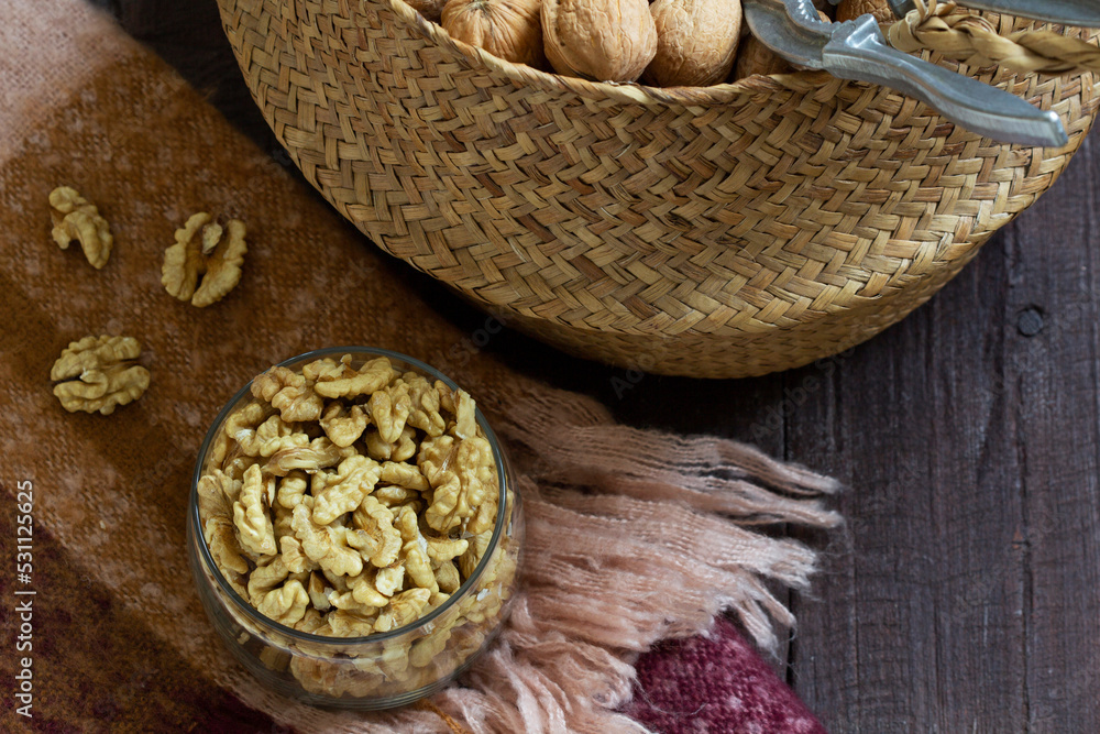 Whole walnuts and a nutcracker in a basket, nut kernels in a jar on a wooden table.