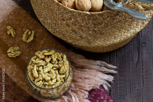Whole walnuts and a nutcracker in a basket, nut kernels in a jar on a wooden table.
