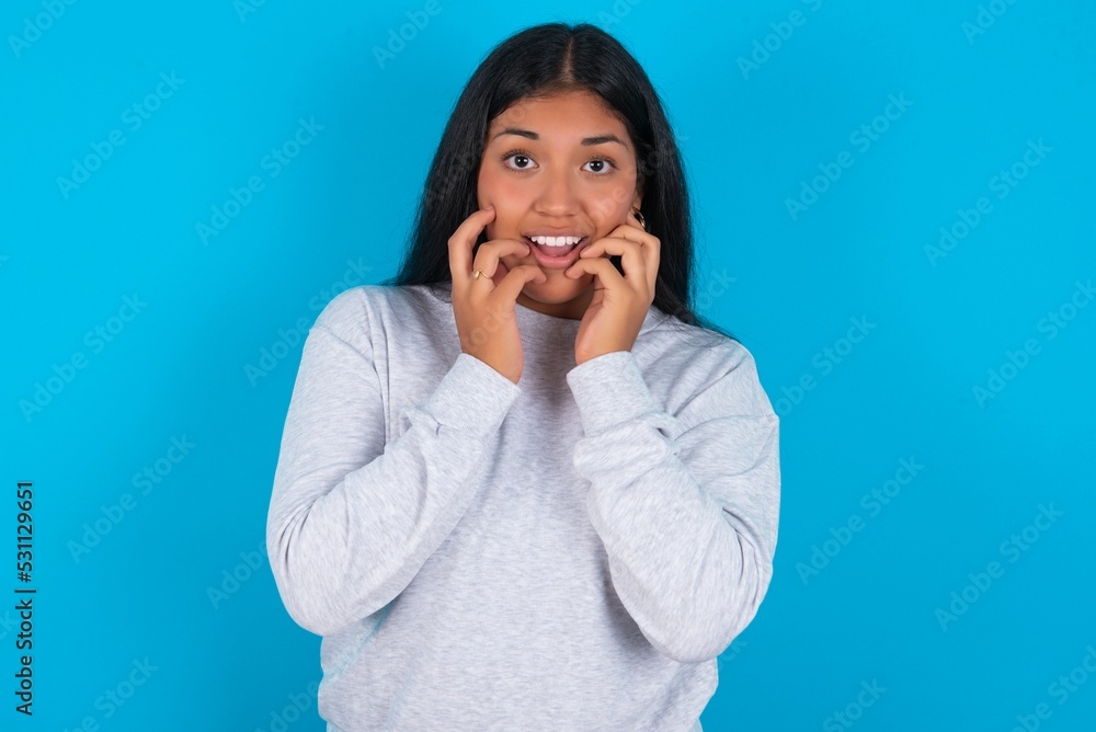 Speechless Young latin woman wearing gray sweater blue background keeps hands near opened mouth reacts to shocking news stares wondered at camera Speechless Young latin woman wearing gray sweater blue background keeps hands near opened mouth reacts to shocking news stares wondered at camera