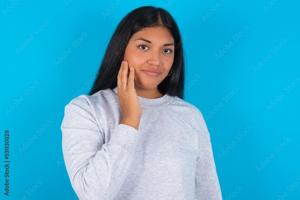 Photo of Young latin woman wearing gray sweater blue background enjoy fresh perfect smooth skin touch face Photo of Young latin woman wearing gray sweater blue background enjoy fresh perfect smooth skin touch face
