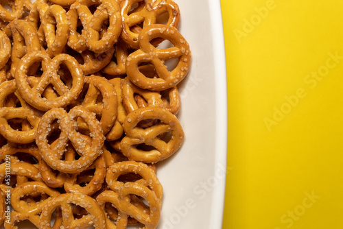 A group of delicious little pretzels on a white plate against a yellow background
