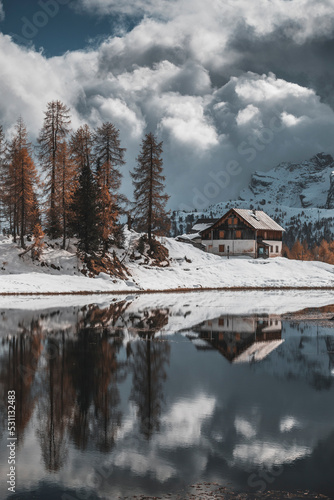 morning by the lake in the late autumn snow covered mountains in italian alps with wooden hut
