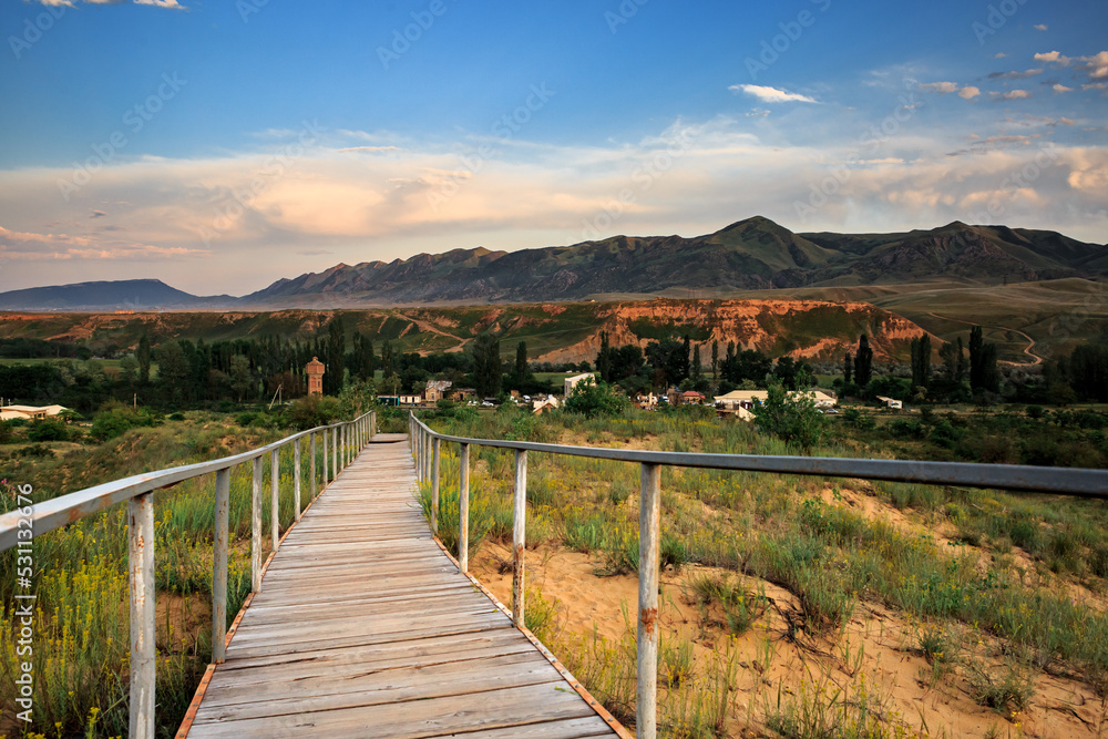 Wooden long road at sunset against the backdrop of mountains and a green landscape.