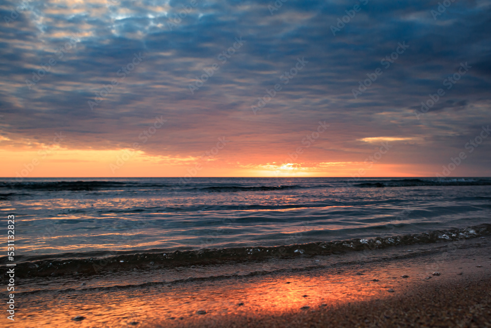 Coast of the Caspian Sea at sunset, pink-orange clouds, water, beach.