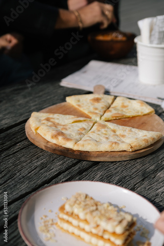 Food in a restaurant: a plate with a sweet dessert, a piece of cake, and megrelian khachapuri pie with cheese bread on the wooden table
