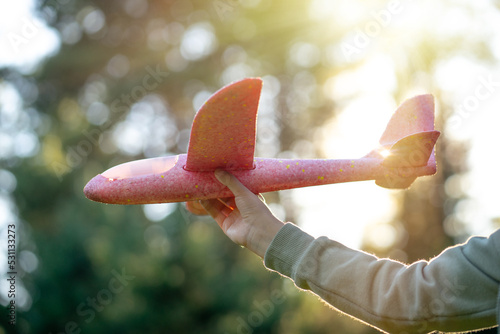 A child holds a toy airplane in his hand against the background of the sun. A game of airplanes.