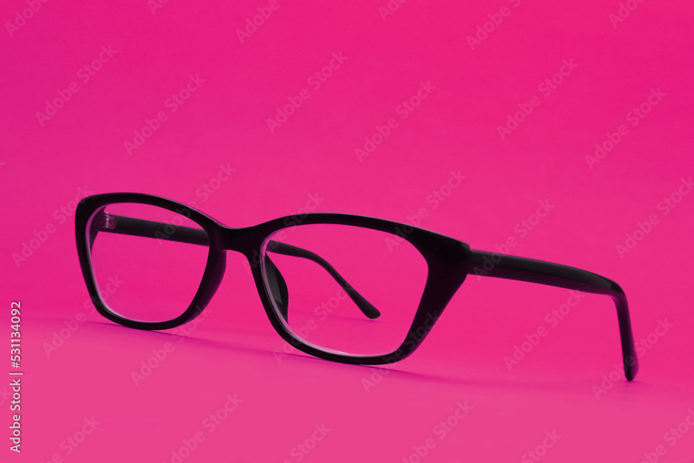 Glasses with diopters in a black frame on a pink background. Shallow depth of field