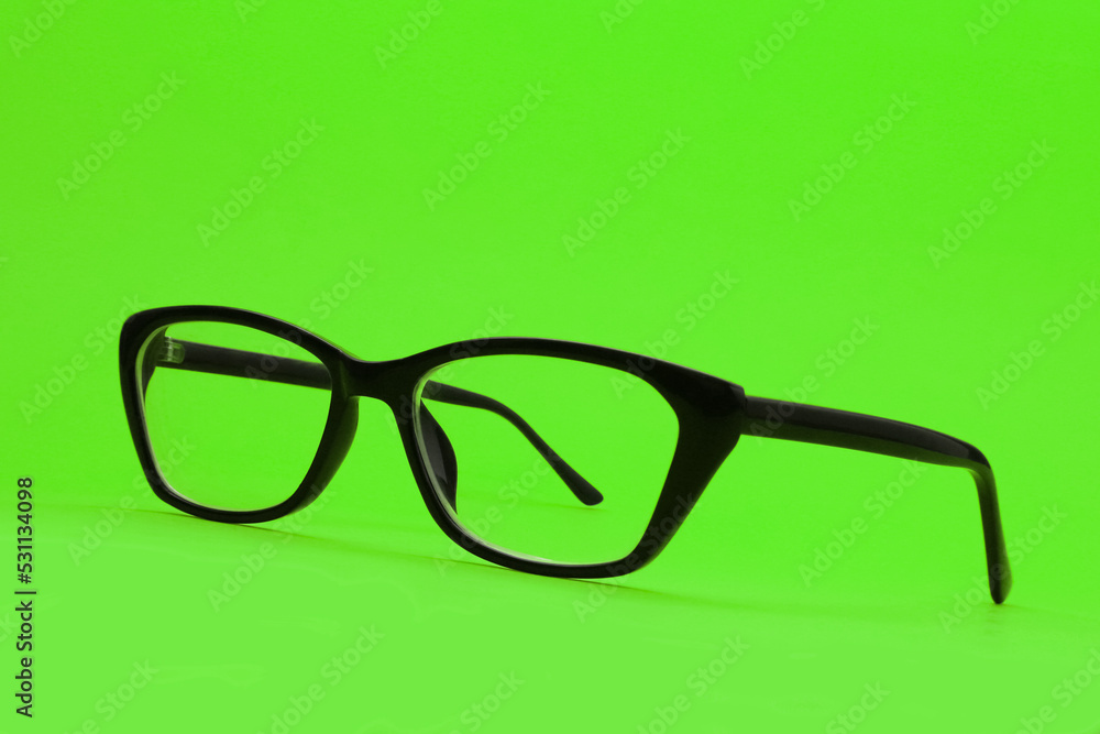 Spectacles with diopters in a black frame on a green background. Shallow depth of field