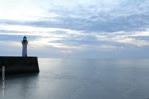 a beautiful seascape at the french coast with a grey smooth sea and a ligthhouse in front