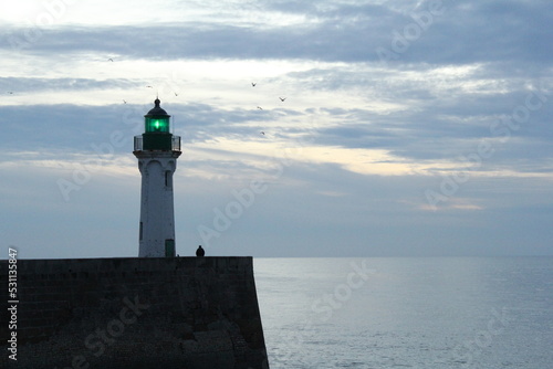 a beautiful seascape in the evening with a lighthouse at the pier in front of a smooth sea and sky with clouds photo