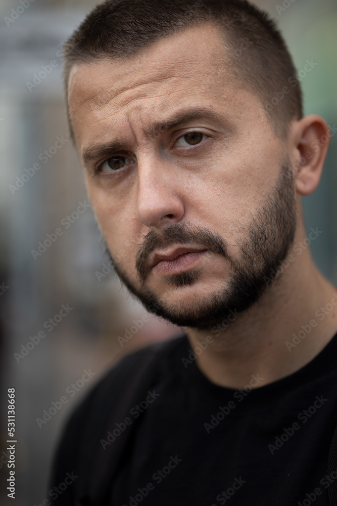 Fototapeta premium Bearded depressed person looks to a camera. Portrait of sad young adult caucasian man. 