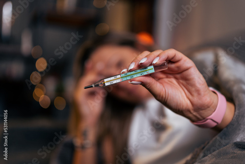 Young Caucasian woman have a cold and high fever while checking body temperature by using digital thermometer. Daily lifestyle health care concept.