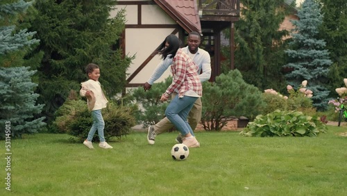 A cheerful family is playing football near the house on the lawn. African dad, Caucasian mom, son.Multiracial Family,Mixed Race,Diverse People,Multiethnic Relations
