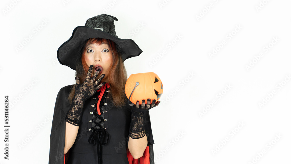 A girl with black and orange hair  in black dress and witch hat is holding pumpkin with wow emotion. Halloween day