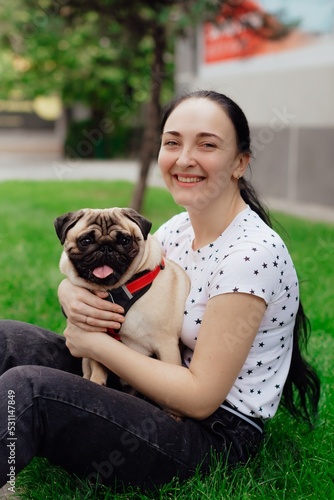 Young girl goes for walk with doggy pug in park. Selective focus.