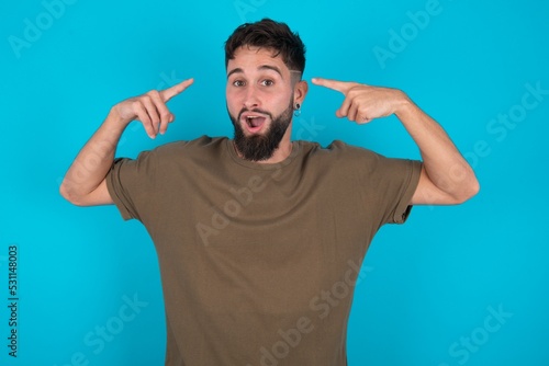 Cheerful young bearded hispanic man wearing casual clothes over blue background demonstrating hairdo
