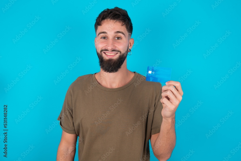 Photo of happy cheerful smiling positive young handsome latin man wearing casual clothes standing over blue background recommend credit card Photo of happy cheerful smiling positive young handsome latin man wearing casual clothes standing over blue background recommend credit card