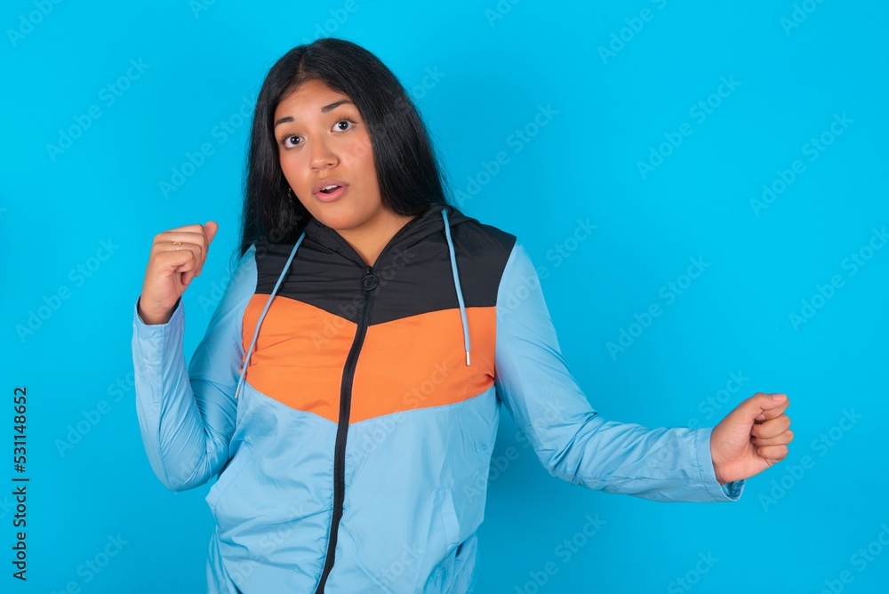 young beautiful woman wearing sport outfit against blue wall, dancing and listening music with headphones. young beautiful woman wearing sport outfit against blue wall, dancing and listening music with headphones.