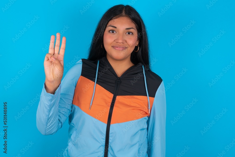 young beautiful latin woman wearing sportswear showing and pointing up with fingers number three while smiling confident and happy. young beautiful latin woman wearing sportswear showing and pointing up with fingers number three while smiling confident and happy.