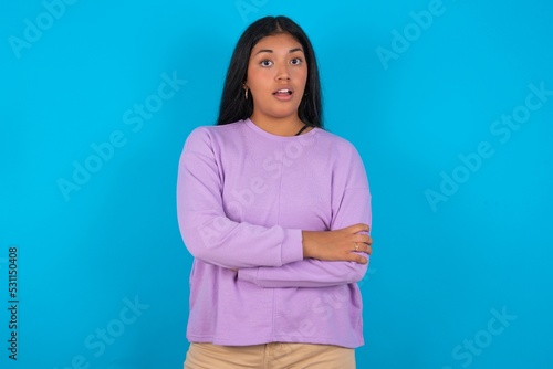 Shocked embarrassed Young beautiful hispanic woman wearing casual clothes over blue background keeps mouth widely opened. Hears unbelievable novelty stares in stupor