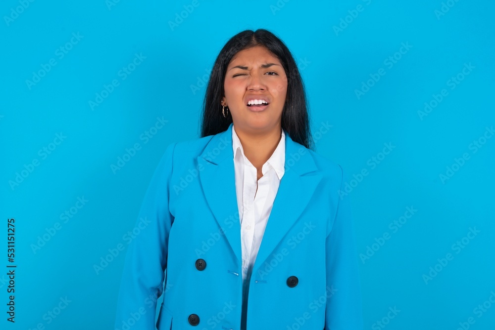 young hispanic businesswoman wearing blue blazer over blue background yawns with opened mouth stands. Daily morning routine young hispanic businesswoman wearing blue blazer over blue background yawns with opened mouth stands. Daily morning routine
