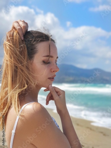 portrait of a woman. A girl with long red hair gathered in a ponytail enjoys nature on the beach during the wind. Close-up portrait of a girl with freckles