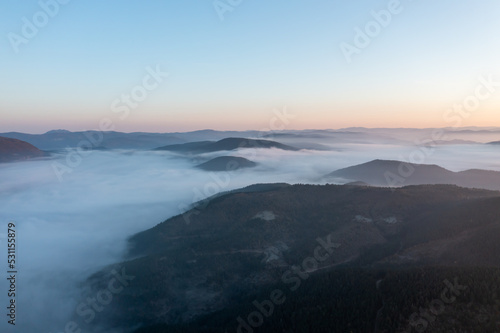 aerial view of morning lights, sun shines over clouds and plateau houses and trees with blue sky and foggy mountains