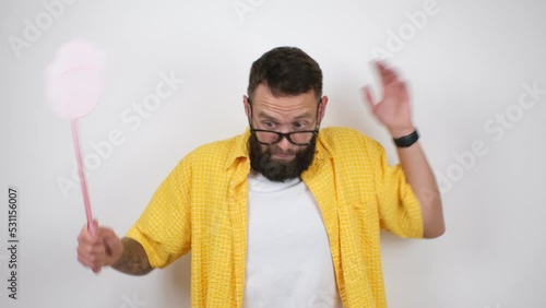 Young caucasian charismatic man holding a fly swatter wanting to kill annoying mosquito or a fly. photo