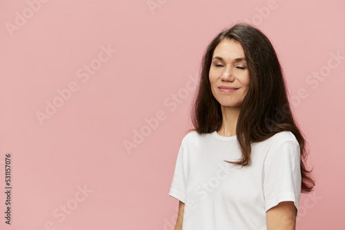 a beautiful cute attractive woman stands on a beige background with long hair, with closed eyes.