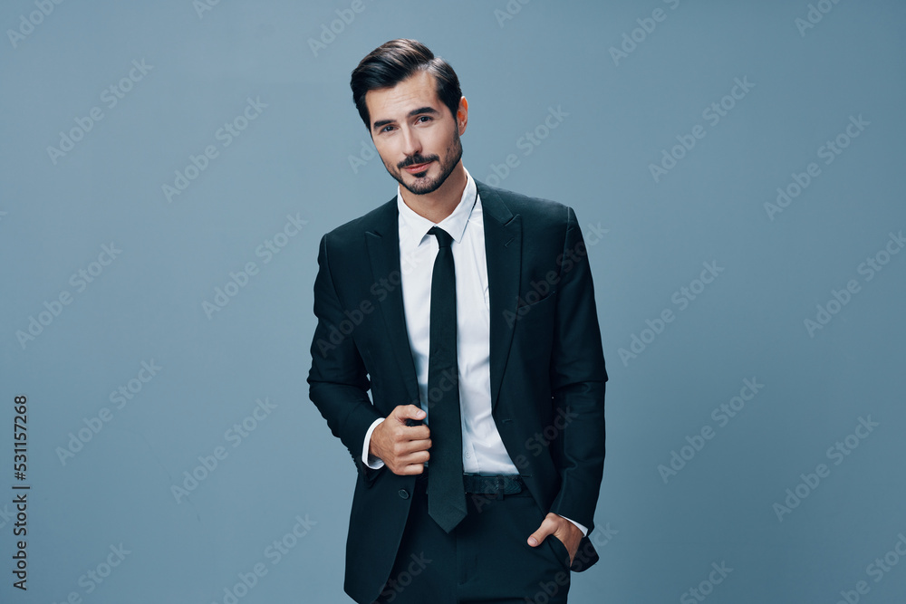 A confident business man smiles and looks at the camera in a black business suit on a blue background brunette with a beard A confident business man smiles and looks at the camera in a black business suit on a blue background brunette with a beard