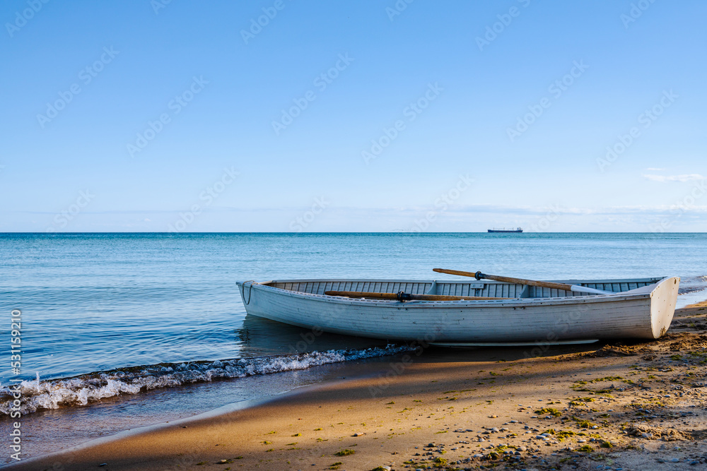 Old row boat on beach with shadow of trees. Calm ocean on the horizon.