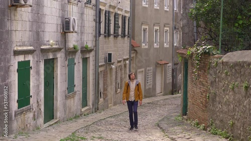 A young man in a yellow jacket is walking along the old street in the city of Risan or Risano. This city is considered the oldest settlement of Boka Kotorska. Travel to Montenegro concept photo