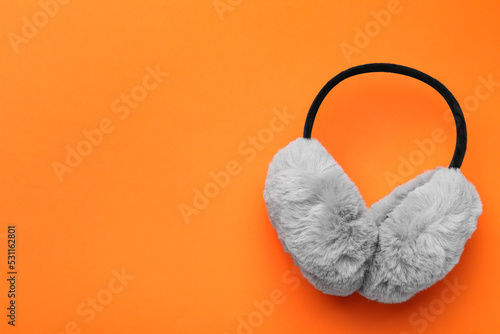 Stylish winter earmuffs on orange background, top view. Space for text