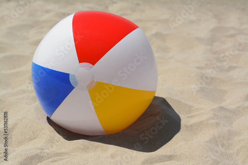 Colorful beach ball on sand, space for text