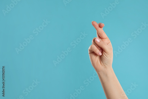 Photography Woman holding fingers crossed on light blue background, closeup with space for text