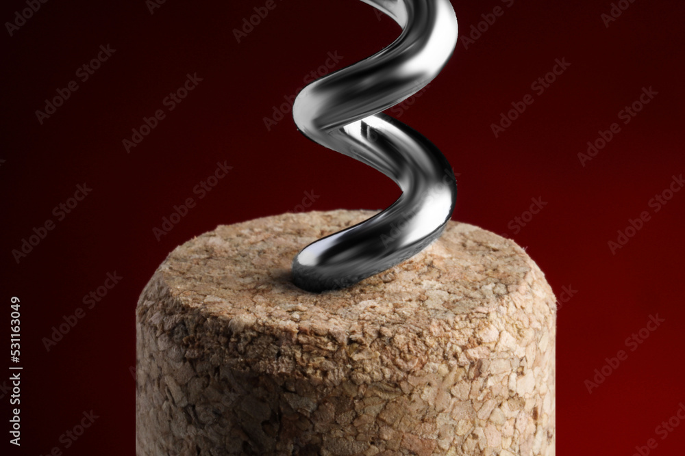 Corkscrew with cork against dark red background, closeup