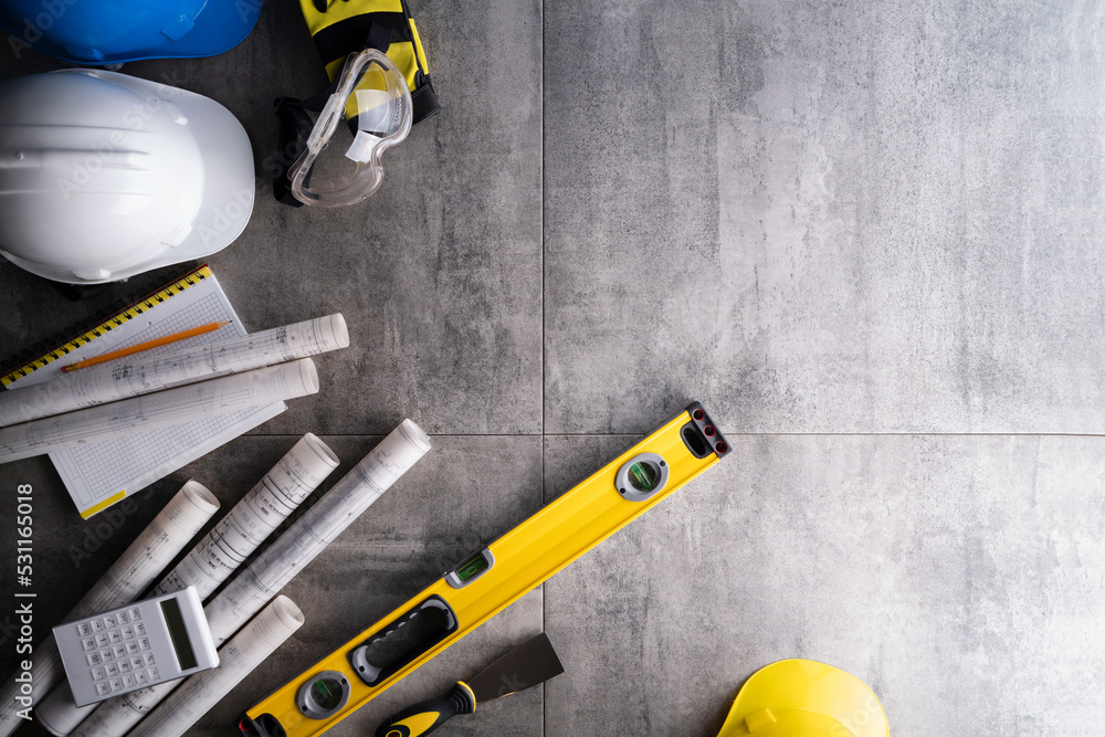 Contractor theme. Plans,  notebook and tool kit of the contractor: yellow hardhat, libella, saw and yardstick  on the gray tiles background.