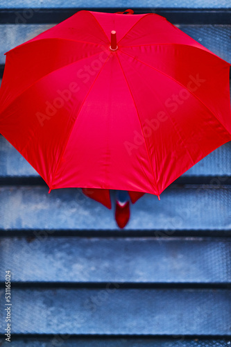 Woman under a red umbrella walking down the stairs to the underground. Business executive woman concept.
