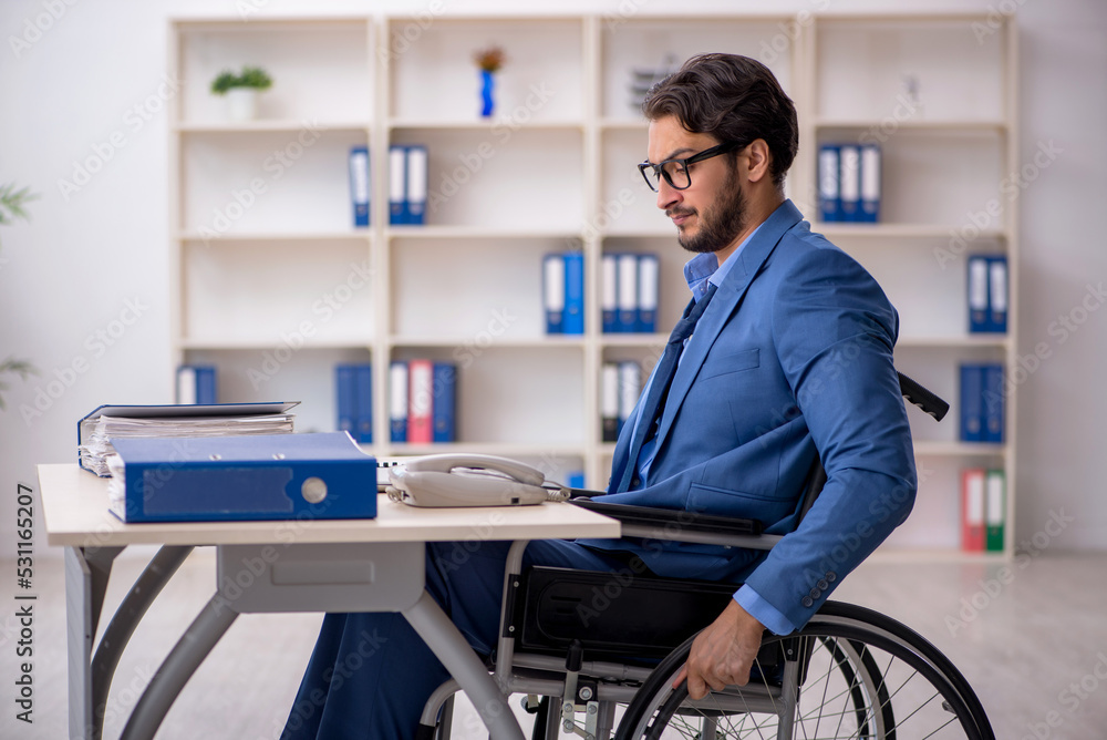 Young male employee in wheel-chair sitting in the office Young male employee in wheel-chair sitting in the office