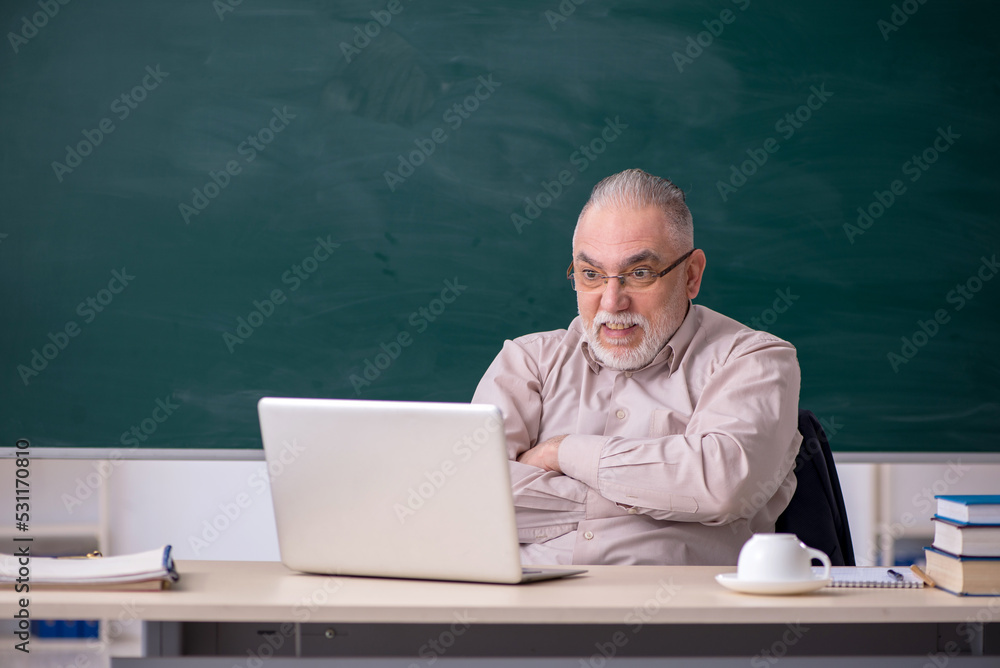 Old male teacher in front of blackboard Old male teacher in front of blackboard