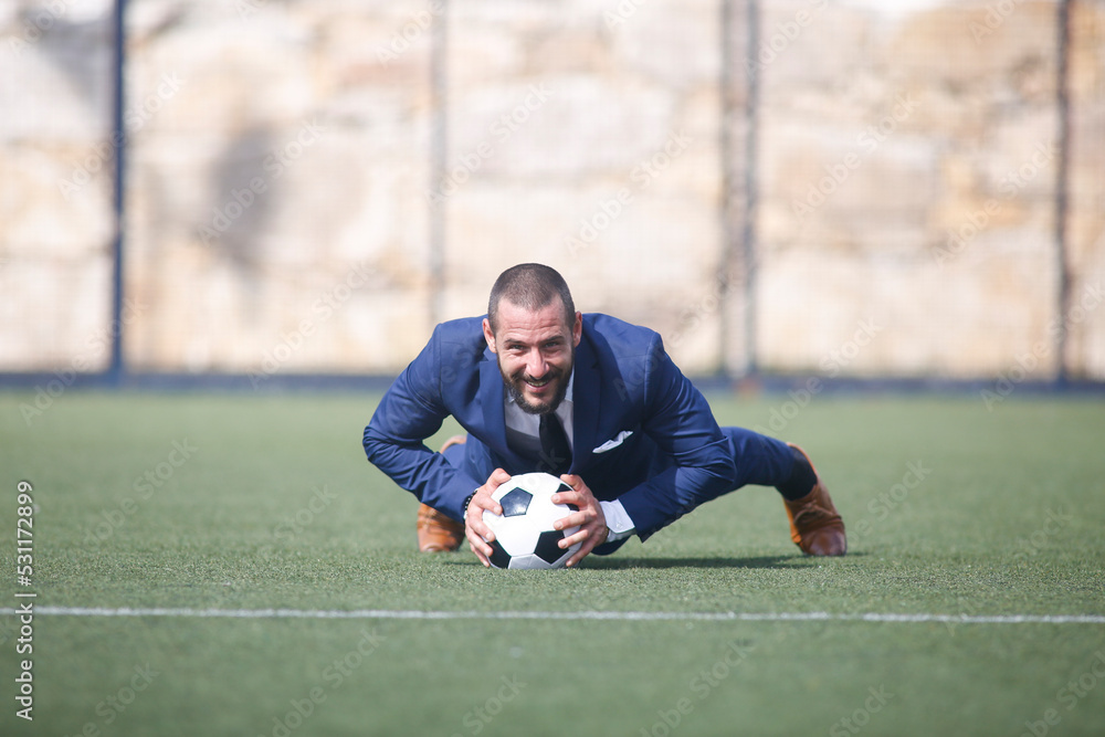 flexed businessman leaning on a ball inside a soccer field flexed businessman leaning on a ball inside a soccer field