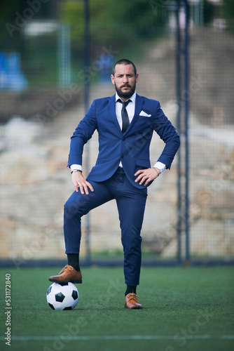business man posing with a ball on his foot inside a soccer field