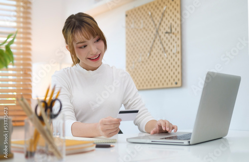 Smiling young woman holding credit card, shopping online, making secure internet payment, browsing banking service on laptop.